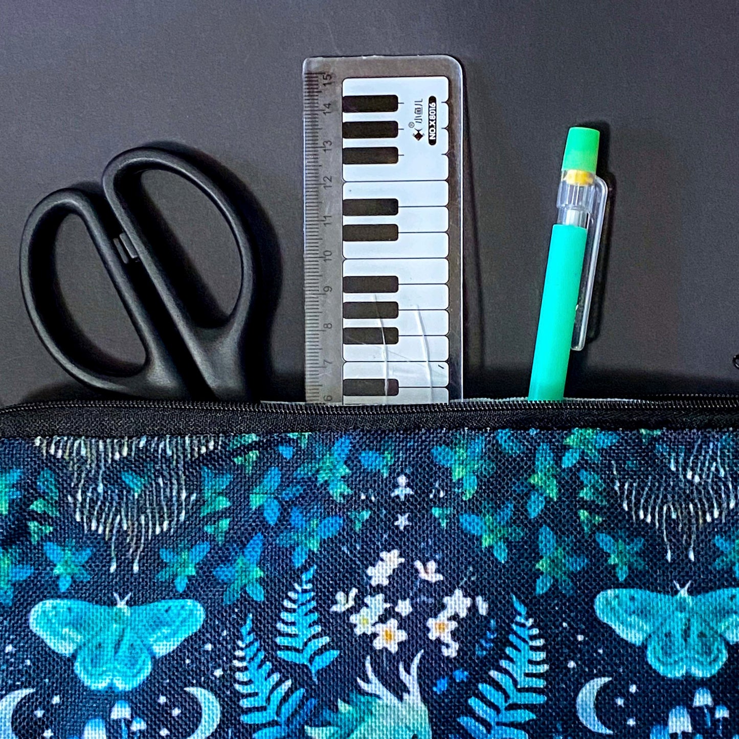 twilight fern dragon fabric zip pouch featuring a turquoise dragon surrounded by ferns, butterflies, flowers, mushrooms and crescent moons on a black background. turquoise, teal and mint green cosmetic bag. 