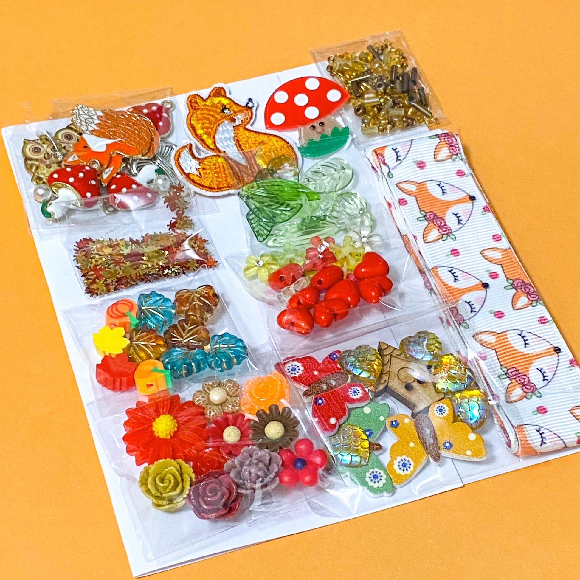autumn fox craft bundle with grosgrain ribbon, beads, enamel charms, sequins and buttons in a cellophane pack on an orange background