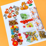 autumn fox craft bundle with grosgrain ribbon, beads, enamel charms, sequins and buttons in a cellophane pack on an orange background
