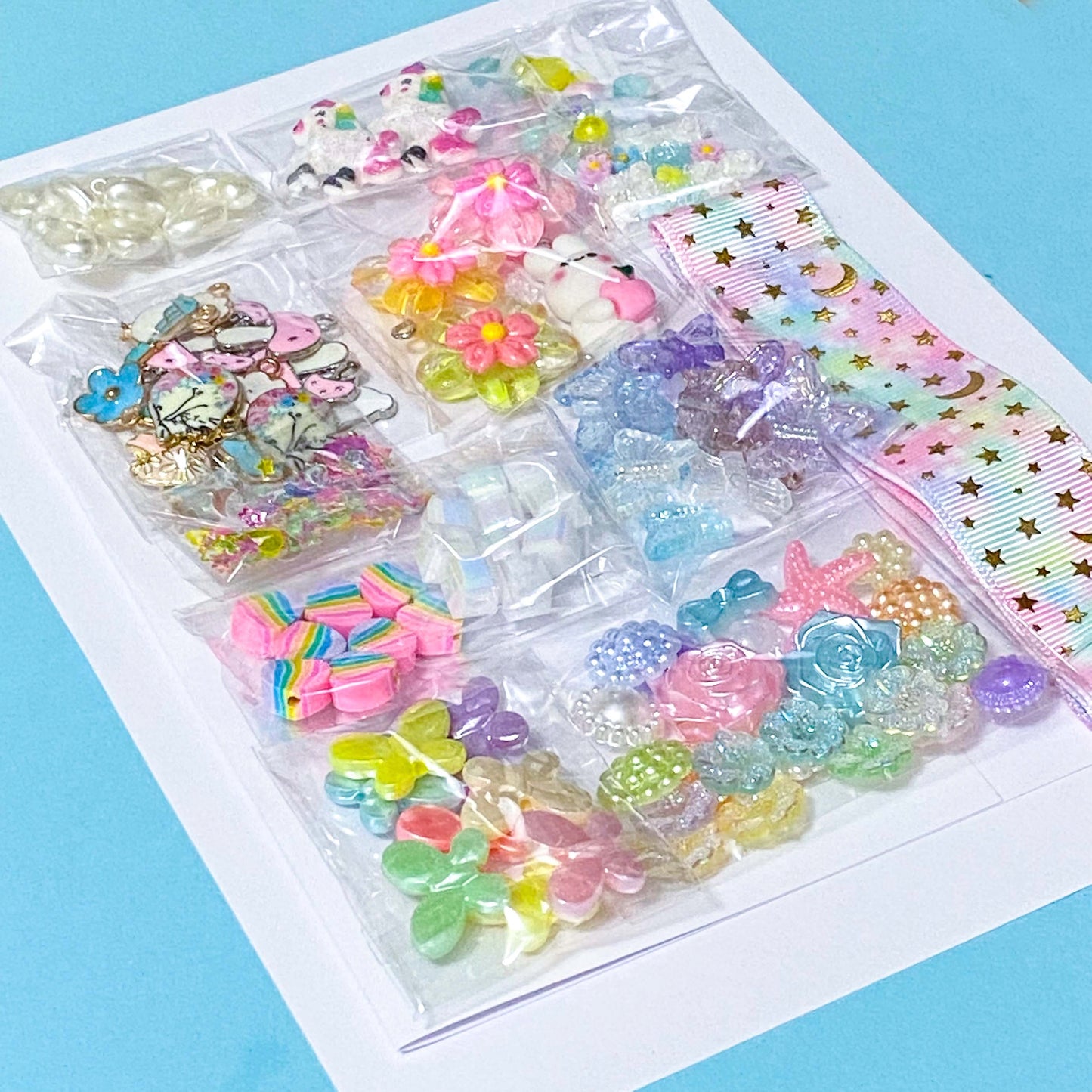craft bundle with a kawaii cute pastel theme with beads, flatbacks, enamel charms, sequins and ribbon on a blue background