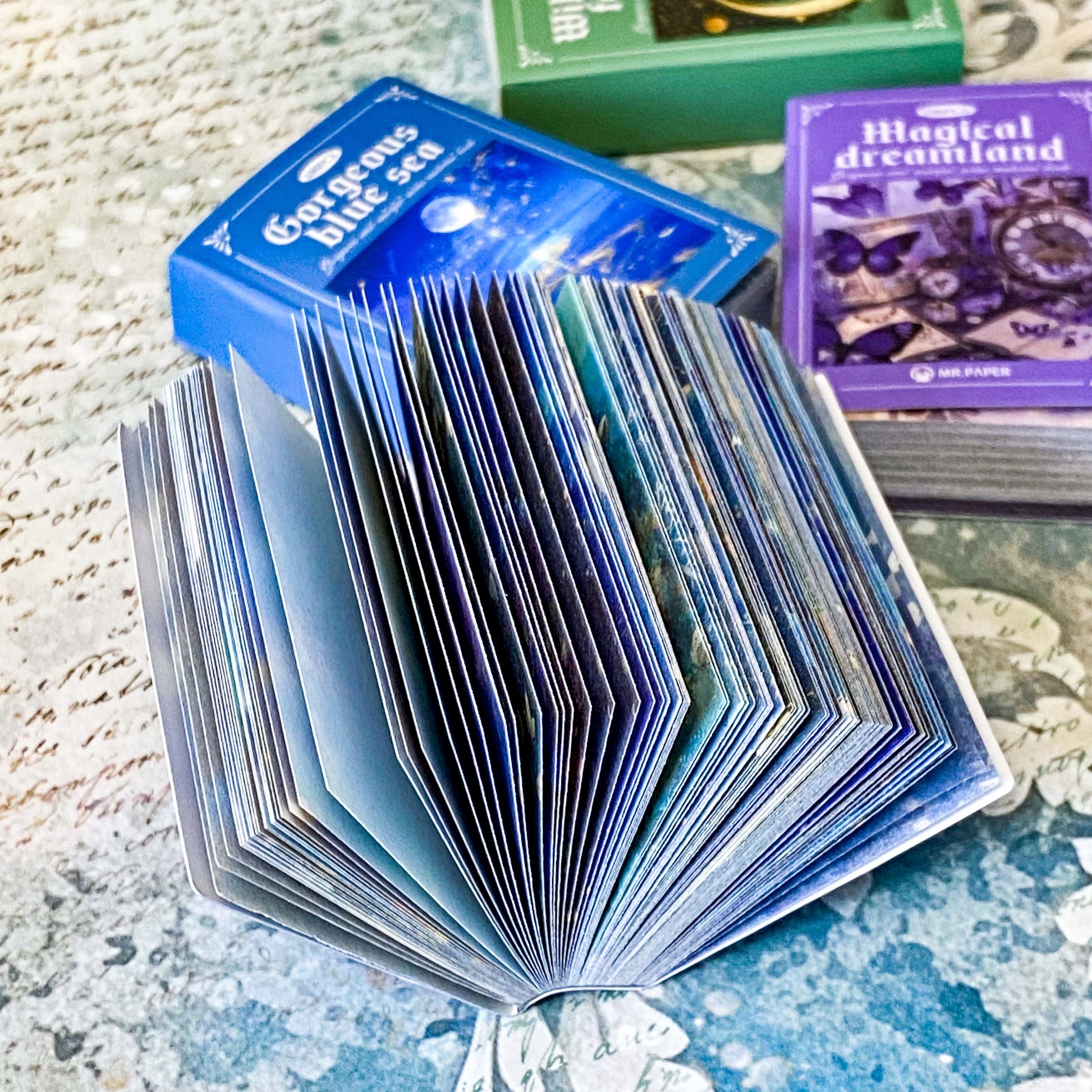 open mini paper book showing scrapbook paper and translucent vellum sheets in blue ocean tones