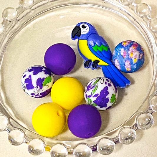 parrot paradise silicone bead bundle featuring a 40mm blue and yellow parrot focal bead with purple, yellow and floral coordinating 16mm silicone beads. Set of . uk craft supplies shop.