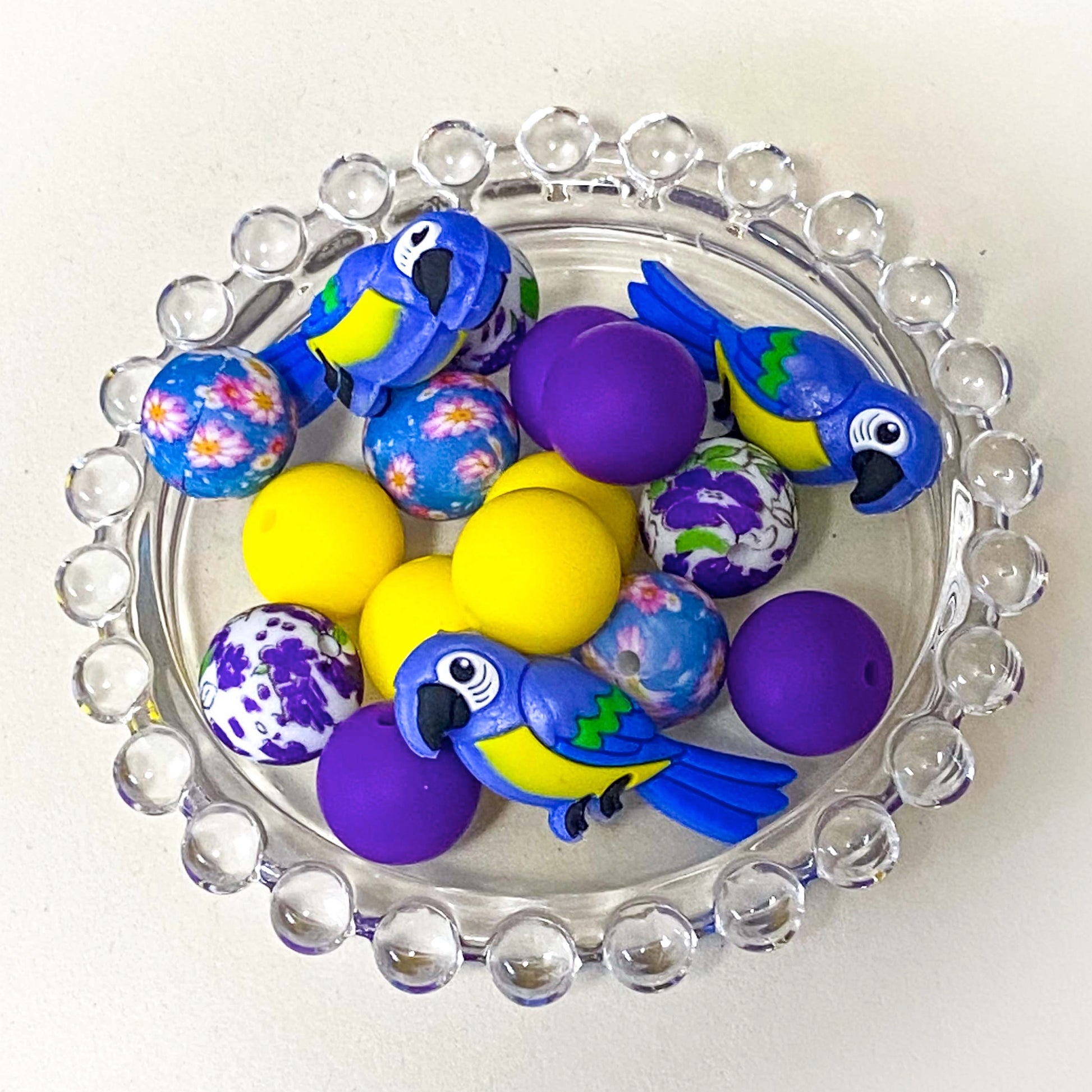parrot paradise silicone bead bundle featuring a 40mm blue and yellow parrot focal bead with purple, yellow and floral coordinating 16mm silicone beads. Set of . uk craft supplies shop.