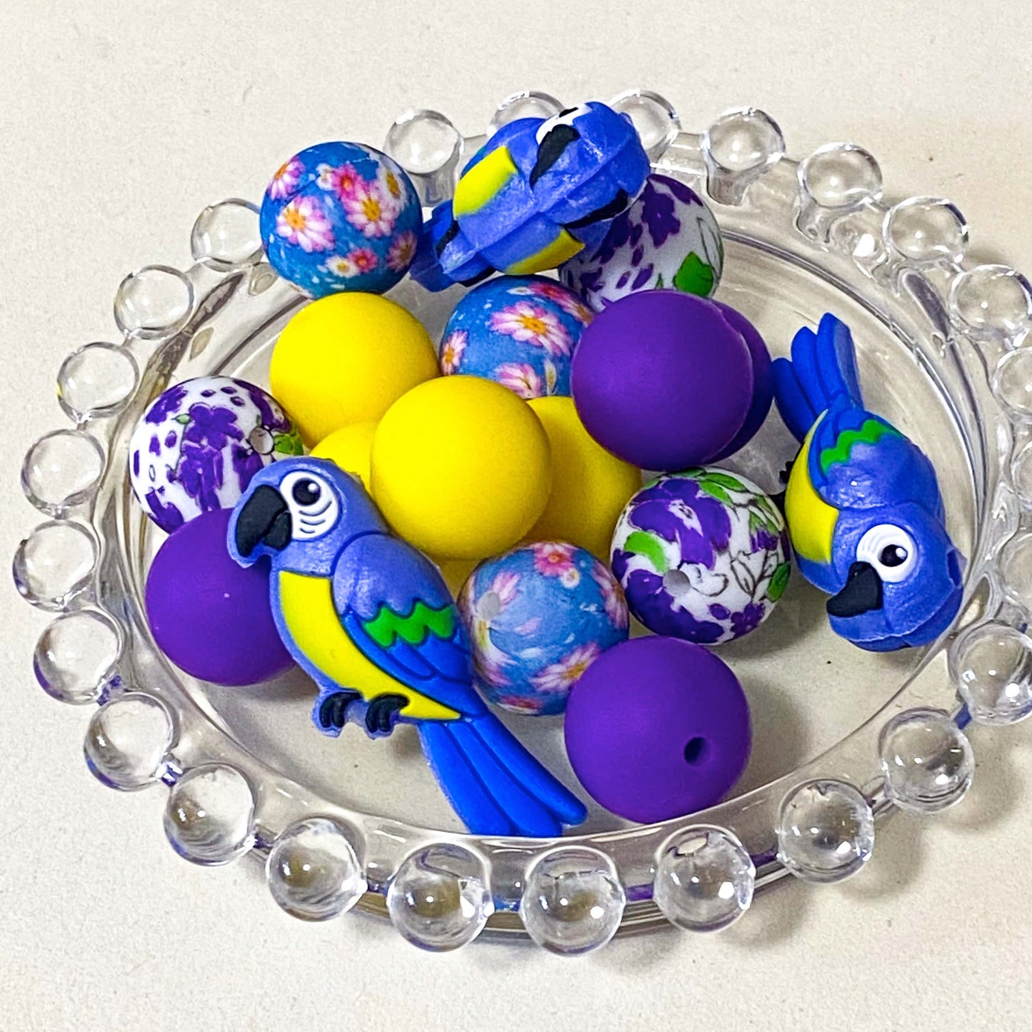 parrot paradise silicone bead bundle featuring a 40mm blue and yellow parrot focal bead with purple, yellow and floral coordinating 16mm silicone beads. Set of . uk craft supplies shop.