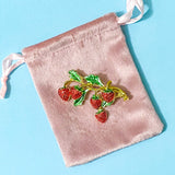 Brooch with red strawberries and green leaves on a pink velvet bag against a blue background