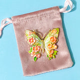 Butterfly-shaped brooch with floral design on a pink velvet bag against a blue background