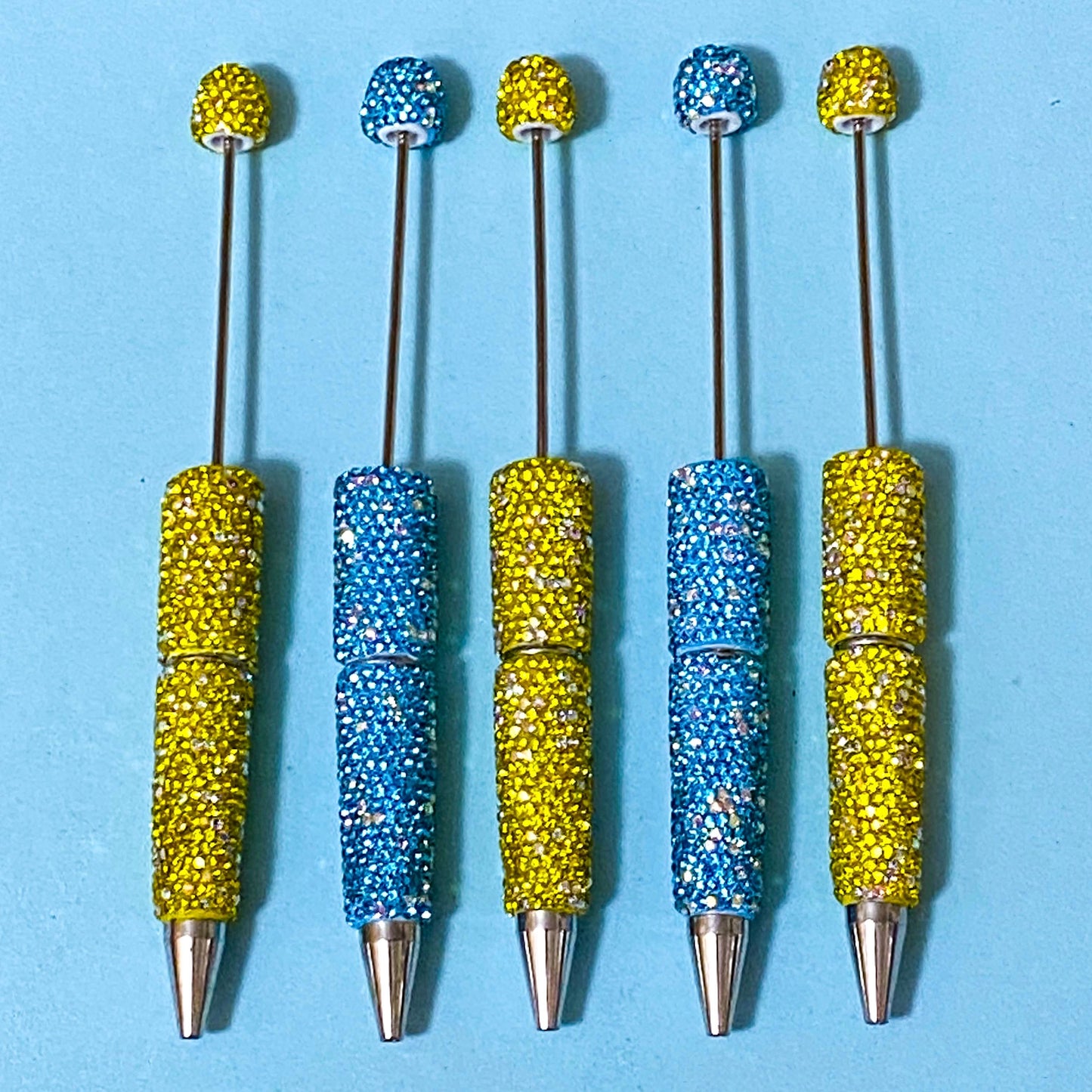 sparkly rhinestone encrusted lemon yellow and turquoise blue pen blanks for making beaded pens on a blue background