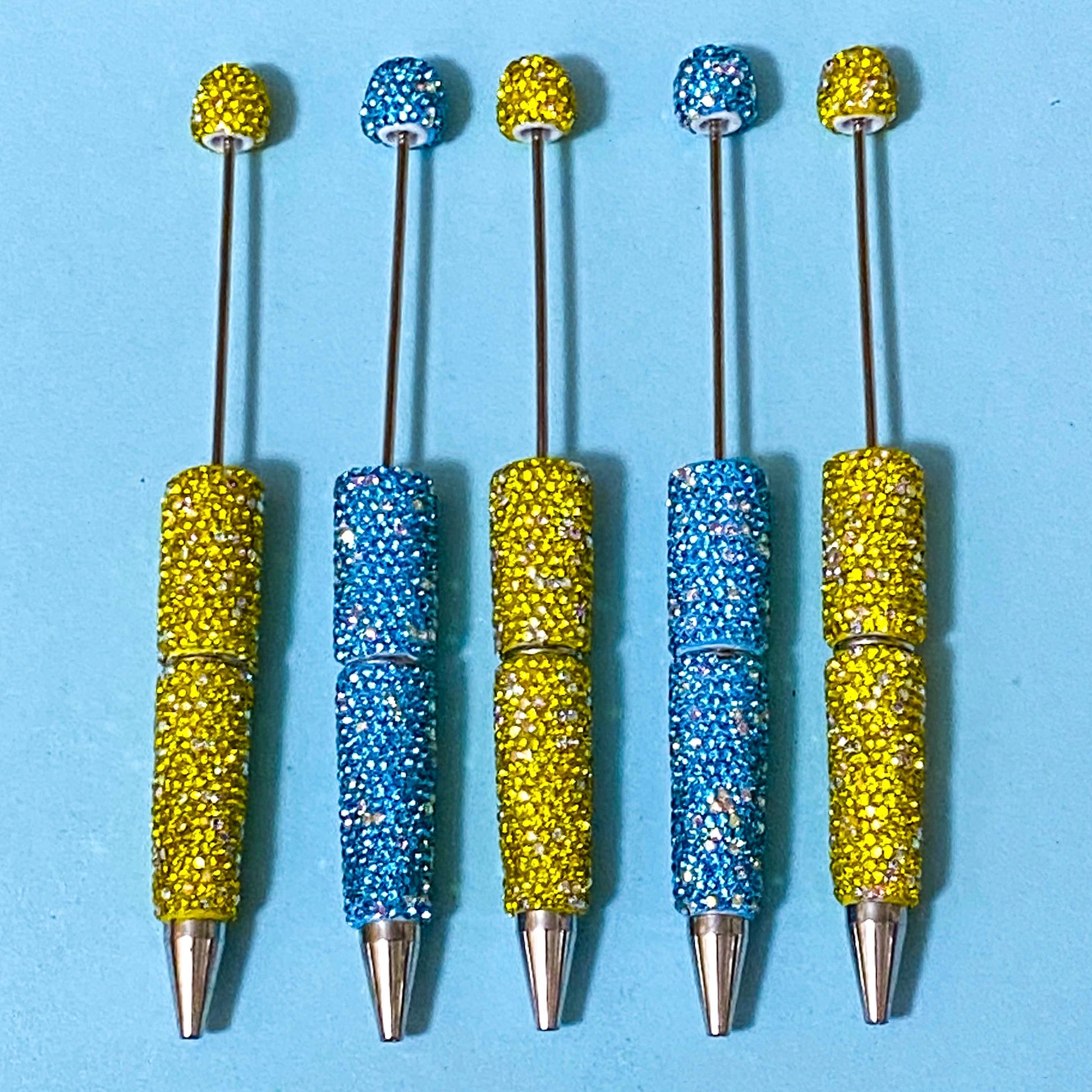 sparkly rhinestone encrusted lemon yellow and turquoise blue pen blanks for making beaded pens on a blue background