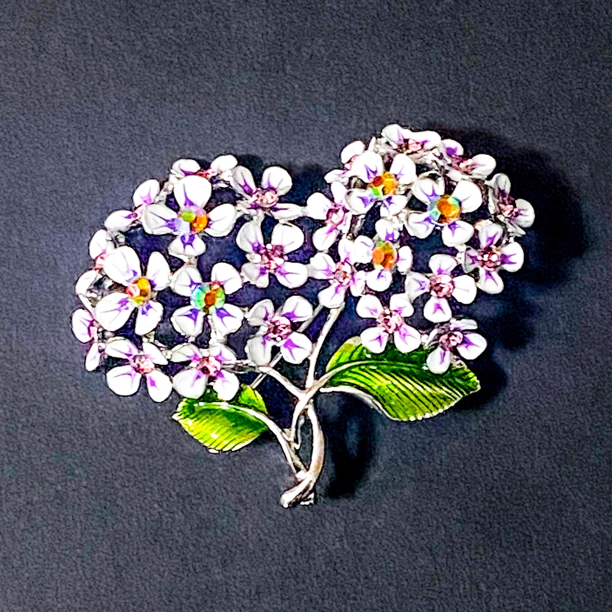 Floral hydrangea lilac and pink sparkly brooch with white flowers and green leaves on a dark background