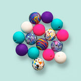 Colourful silicone galaxy themed beads on a clear glass plate with a blue background