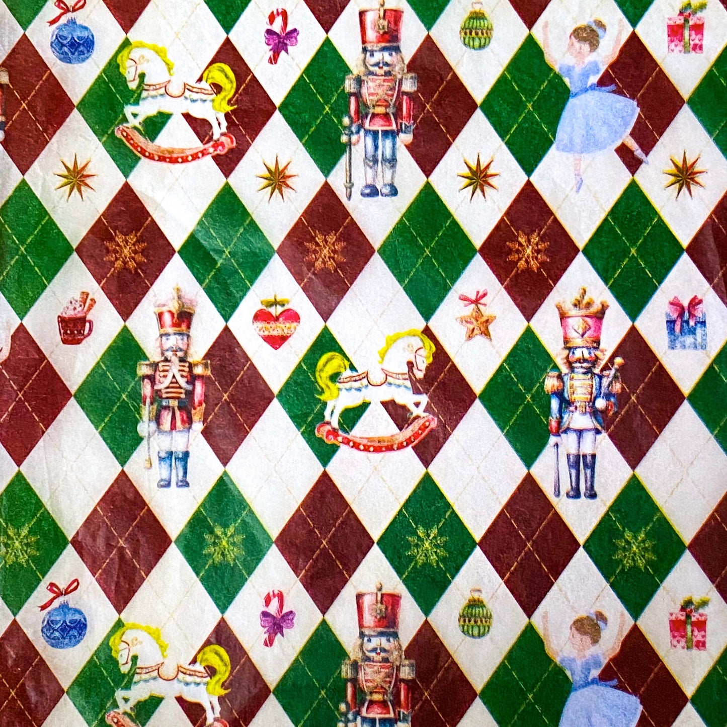 tissue paper with a pattern of nutcracker suite with Clara and rocking horse and tin soldier, on a dark red, green and cream argyle harlequin background.