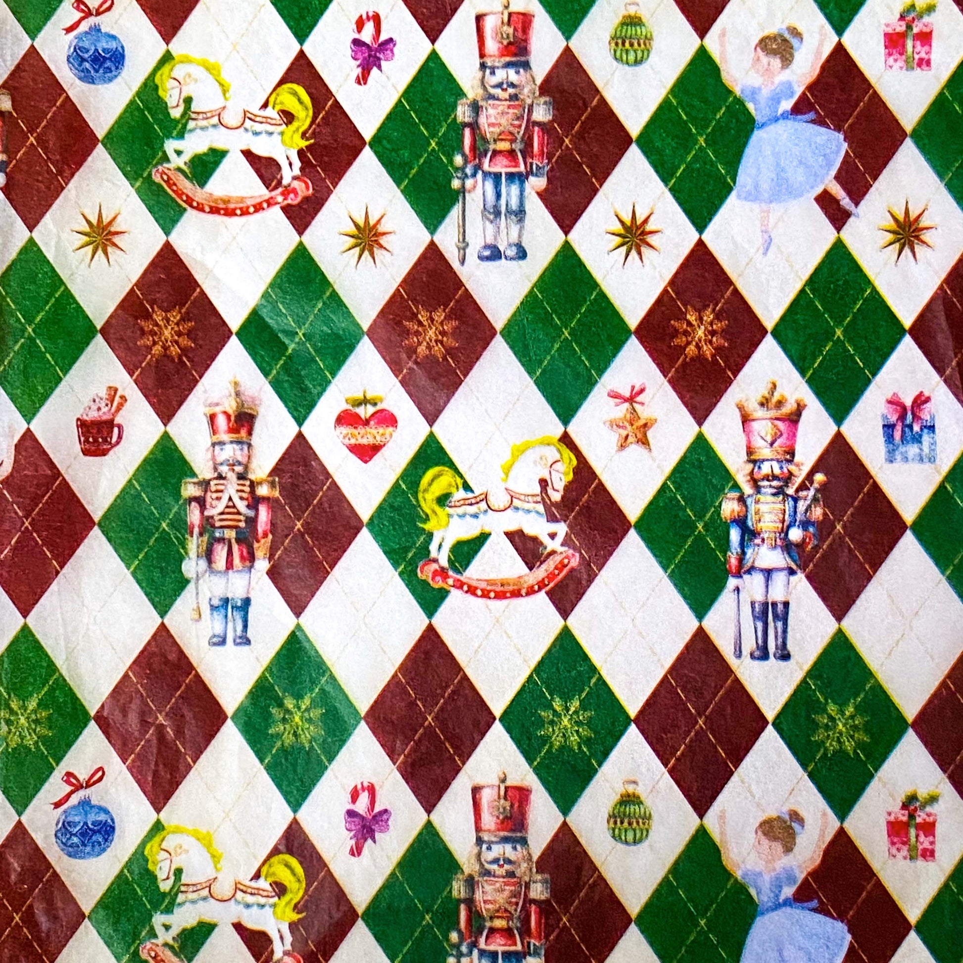 tissue paper with a pattern of nutcracker suite with Clara and rocking horse and tin soldier, on a dark red, green and cream argyle harlequin background.