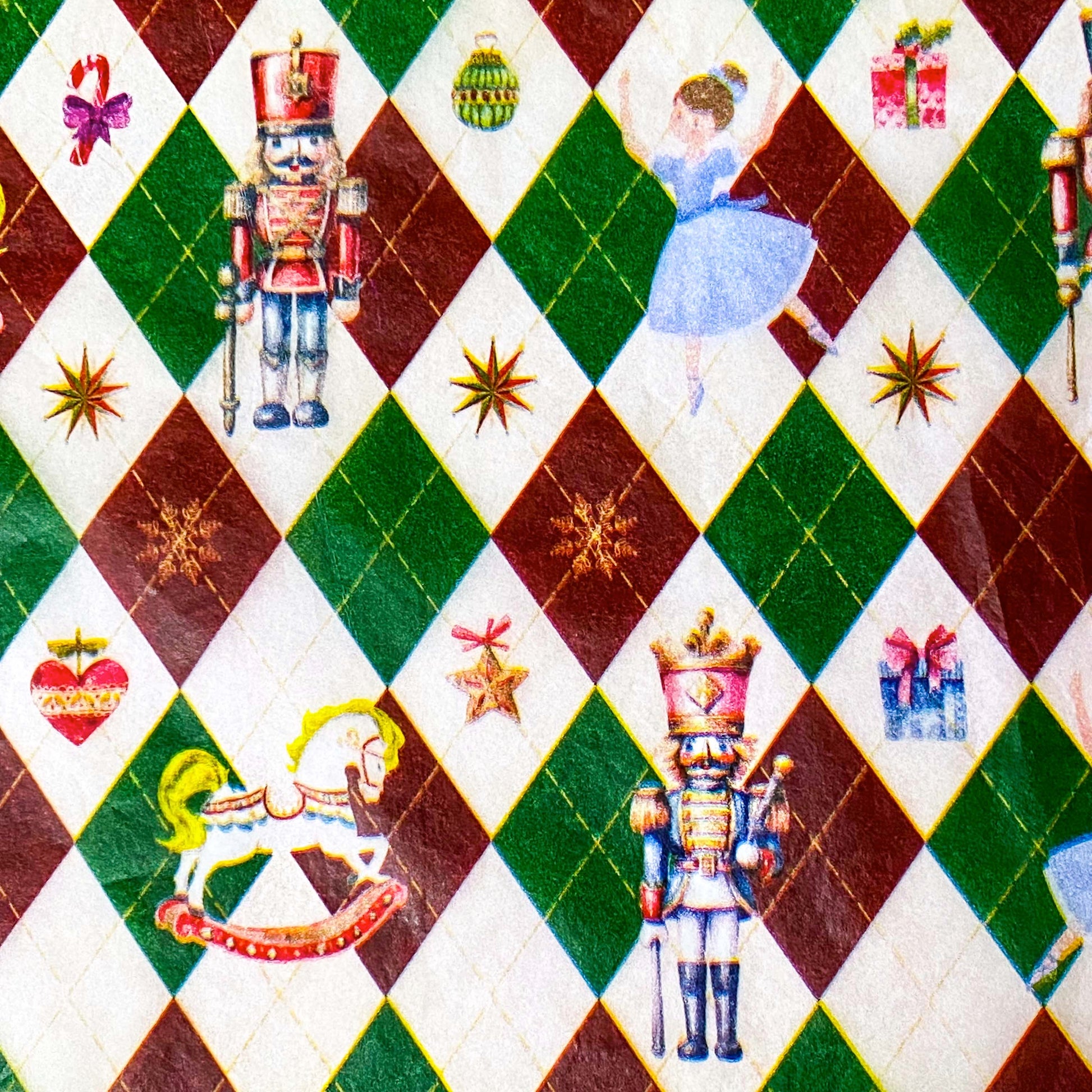 tissue paper with a pattern of nutcracker suite with Clara and rocking horse and tin soldier, on a dark red, green and cream argyle harlequin background.