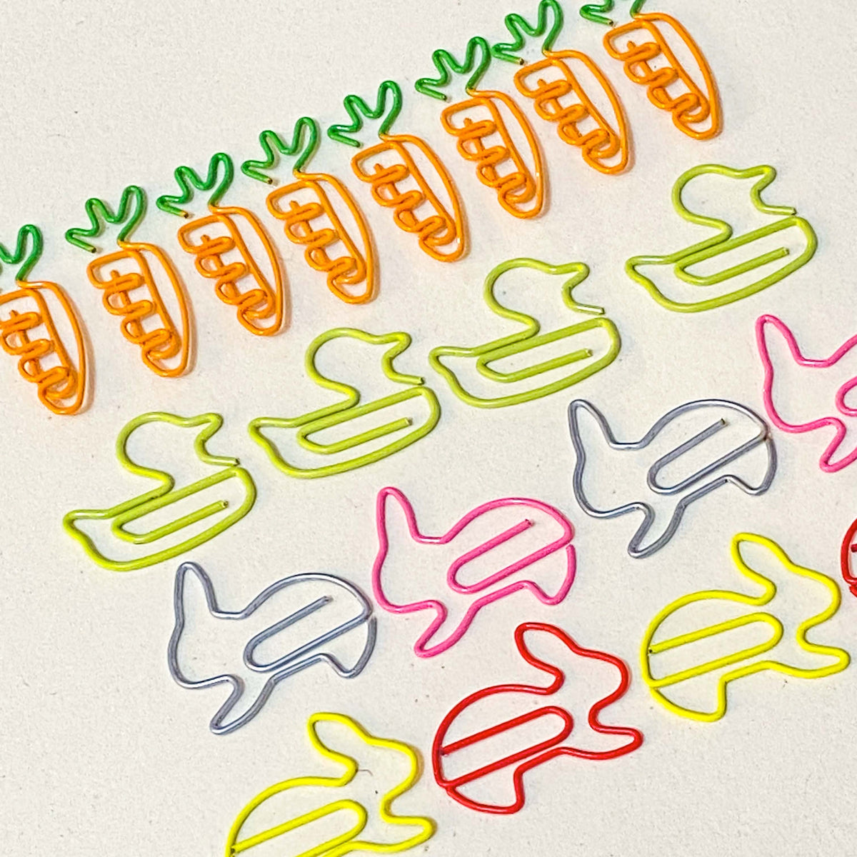 Colourful spring and easter metal jumbo paper clips shaped like carrots, ducks, and rabbits on a beige background