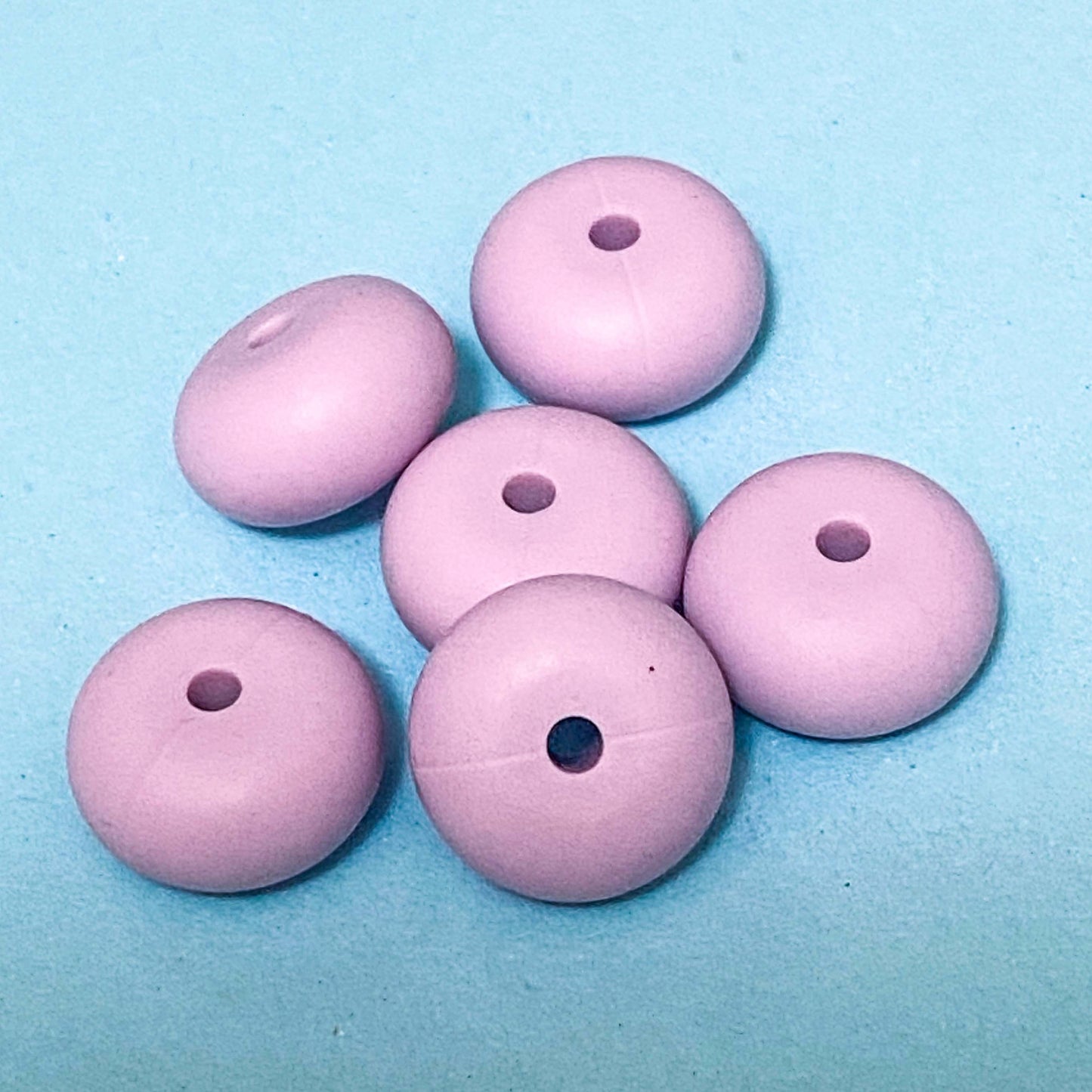 silicone spacer beads with a chunky shape in dusky purple on blue background