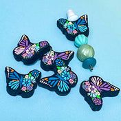 large silicone soft butterfly beads in purple and teal on a blue background