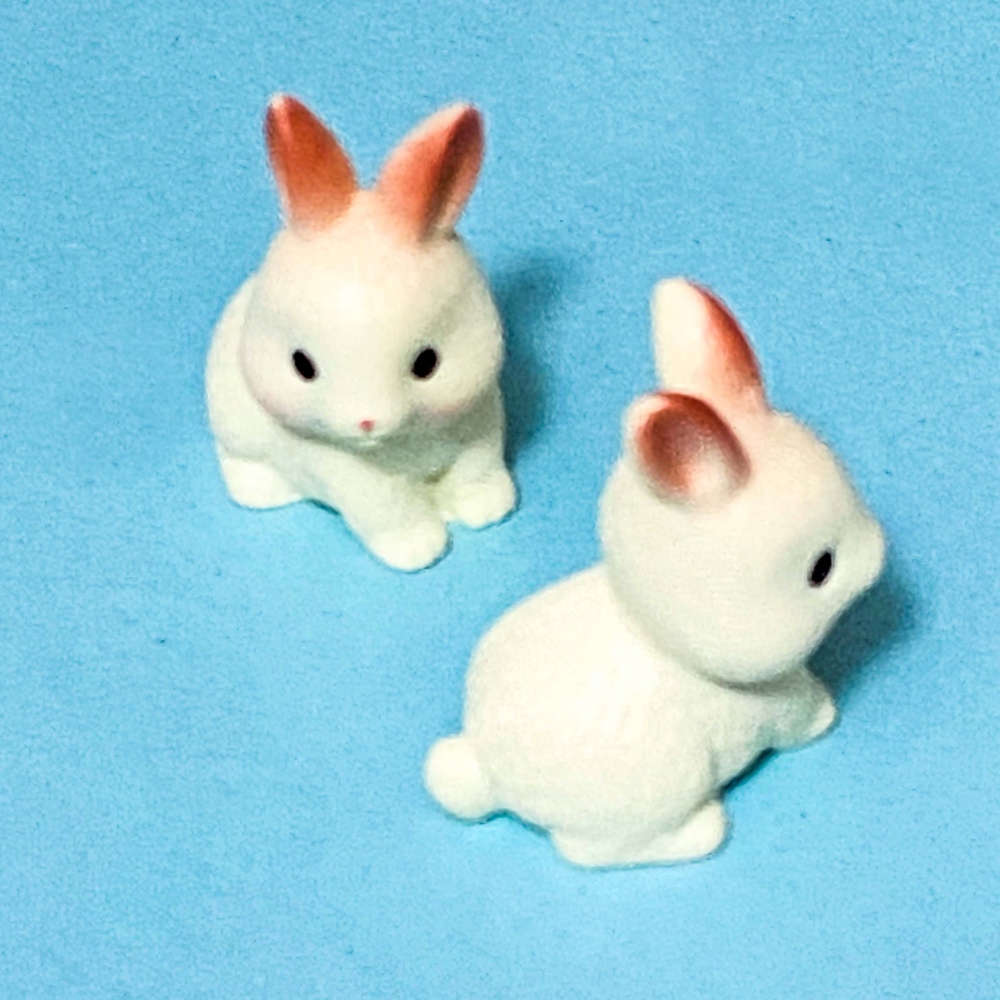 Two small white rabbit figurines with red ears on a blue background