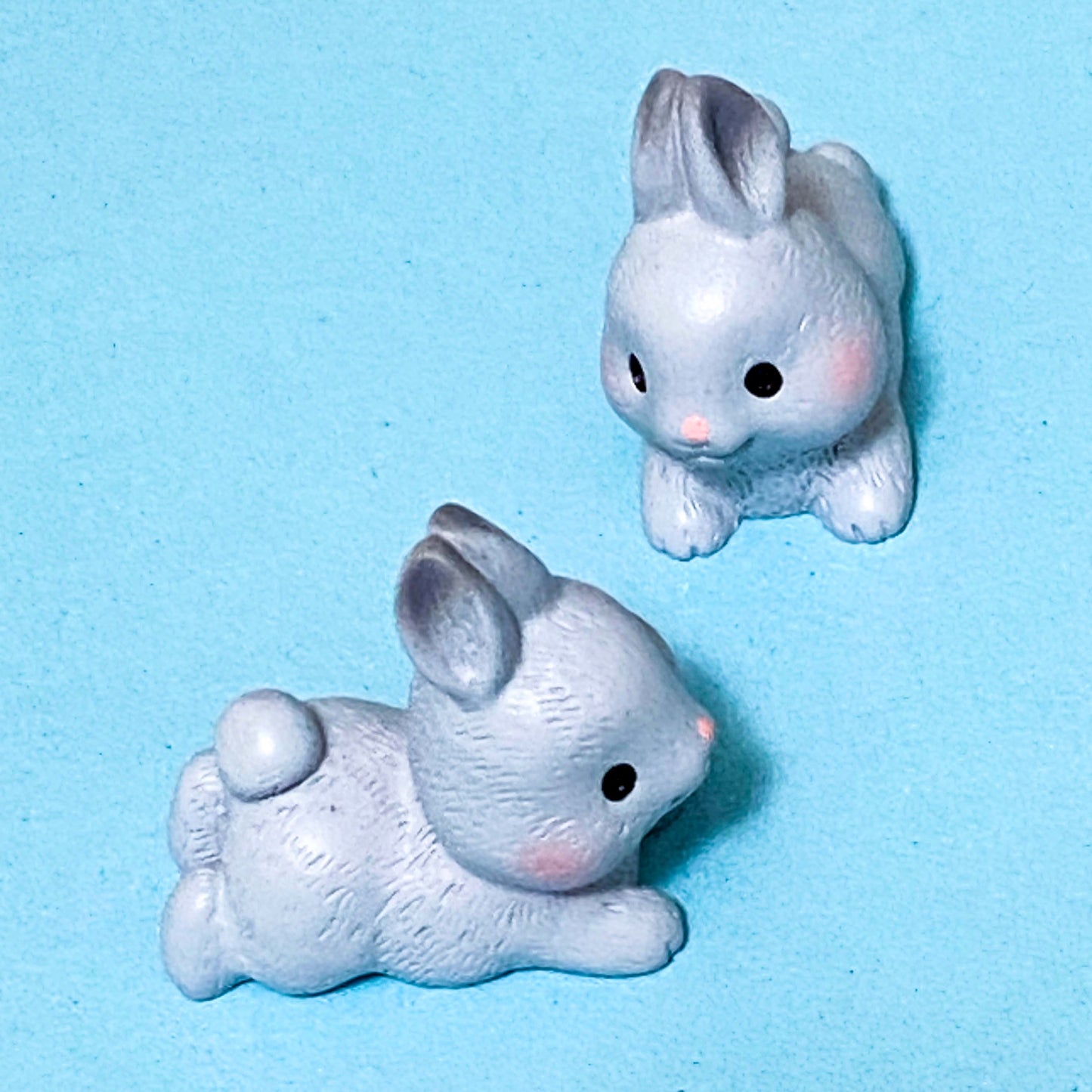 Two small gray rabbit figurines on a light blue background