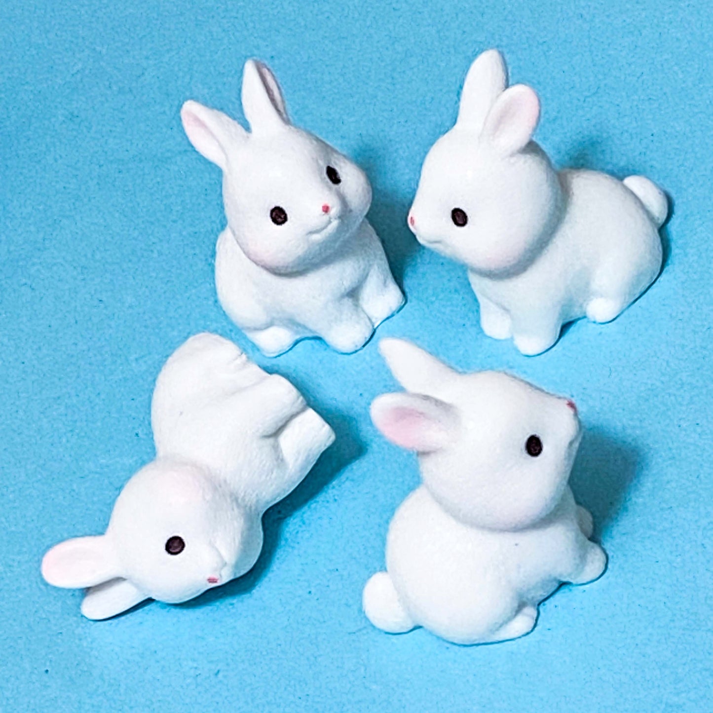 Four resin white rabbit figurines on a blue background