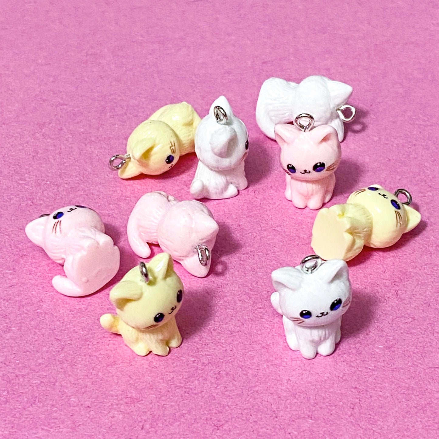 cat resin charms in pink white and pale yellow on a pink background