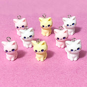 cat resin charms in pink white and pale yellow on a pink background