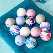 silicone 16mm beads bundle with floral patterned beads and coordinating plain beads in pale pink, light blue, grey and white on a teal velvet bag