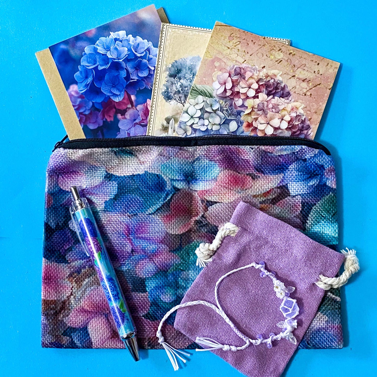 hydrangea whispers midi letterbox gift set with a textured hydrangea pouch, floral ballpoint pen, blank greetings card with kraft envelope, two hydrangeas postcards and an adjustable crystal floral bracelet in a lilac drawstring bag. uk gifts shop.