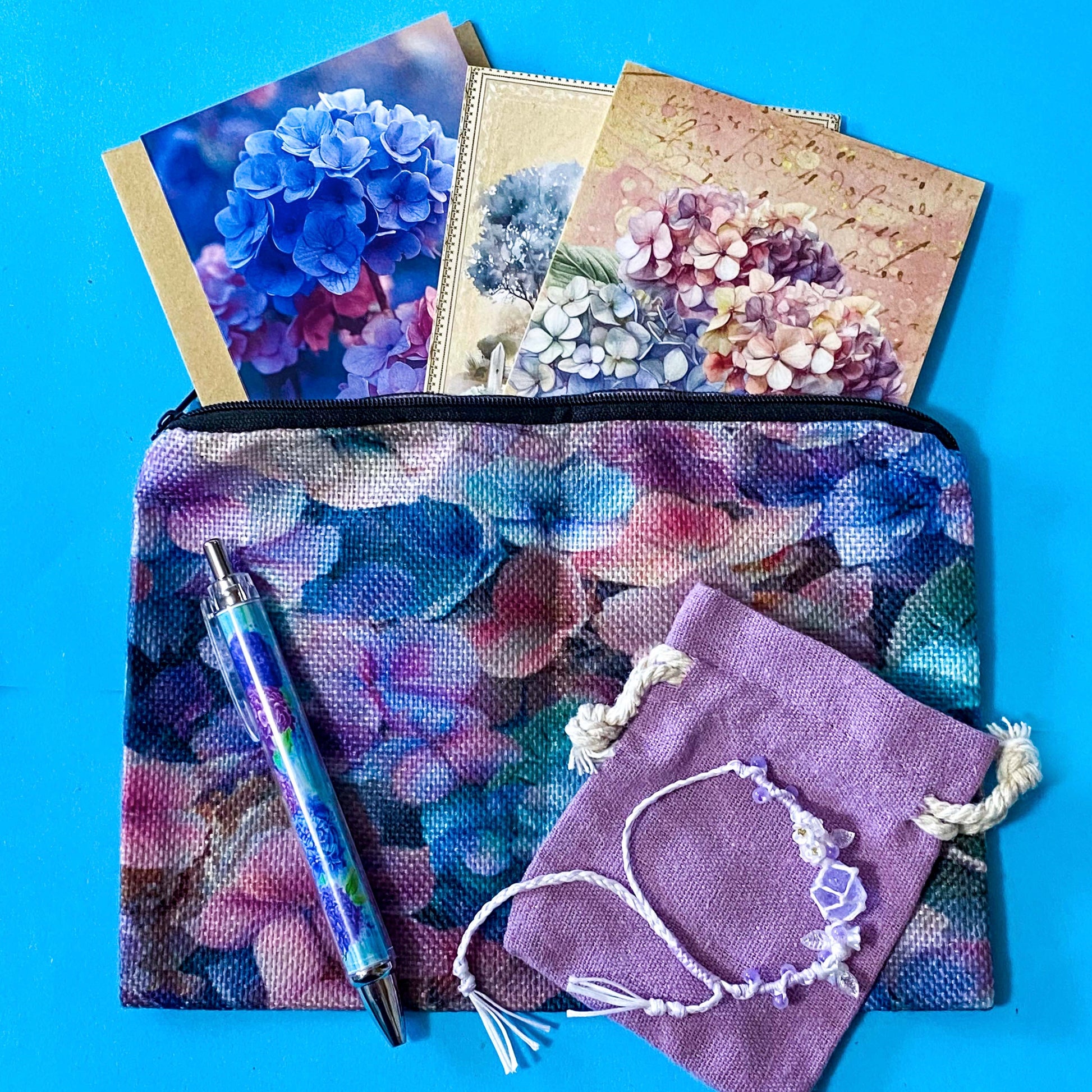 hydrangea whispers midi letterbox gift set with a textured hydrangea pouch, floral ballpoint pen, blank greetings card with kraft envelope, two hydrangeas postcards and an adjustable crystal floral bracelet in a lilac drawstring bag. uk gifts shop.