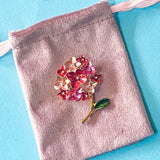 Floral hydrangea brooch on a pink velvet bag against a blue background