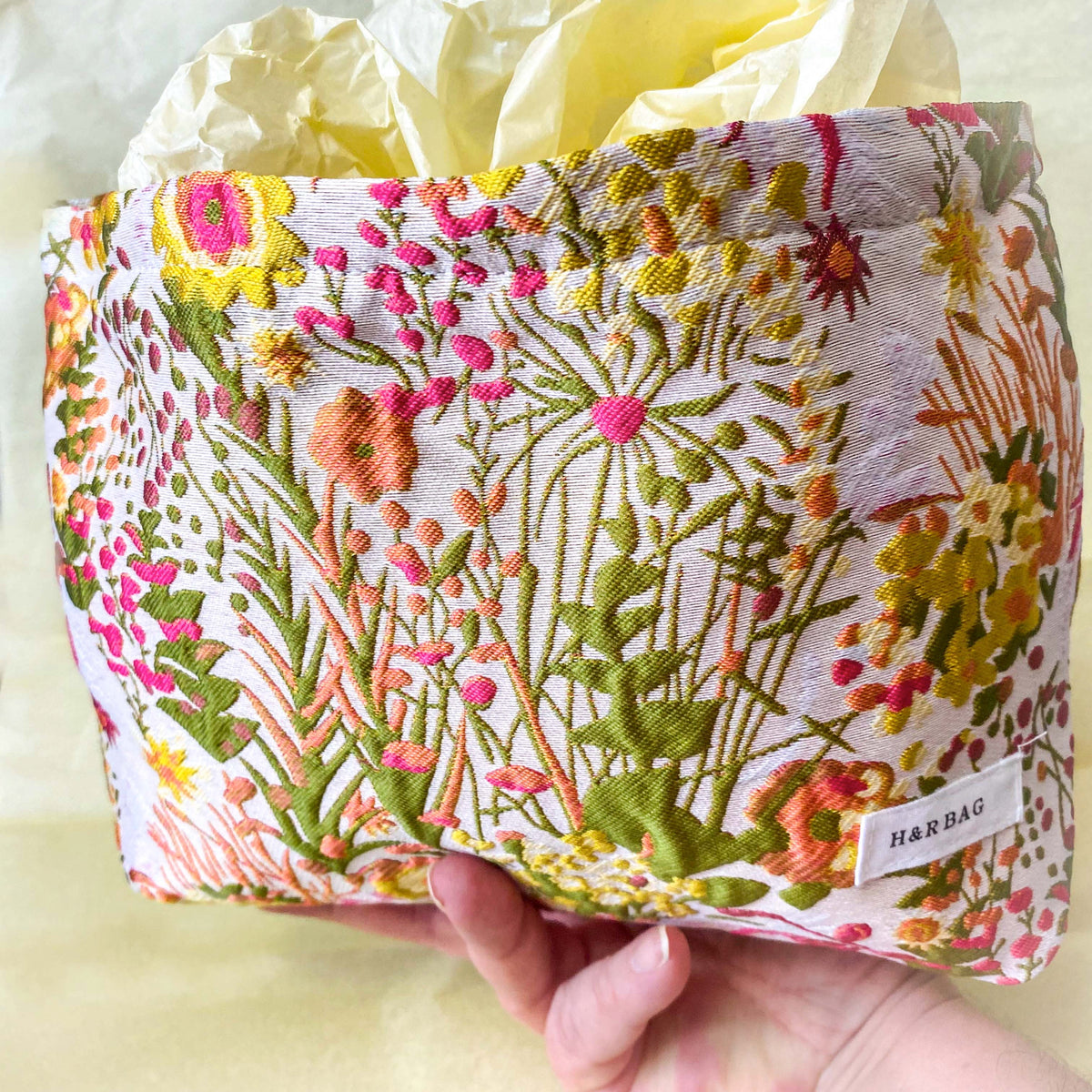 wildflower meadow tapestry pouch with colourful woven floral design including daisies, cream lining, concealed zip closure and gusseted base. Cream, orange, lemon, soft green and white design. Subtle sheen. Large cosmetic bag or toiletry pouch. Uk botanical gift shop.