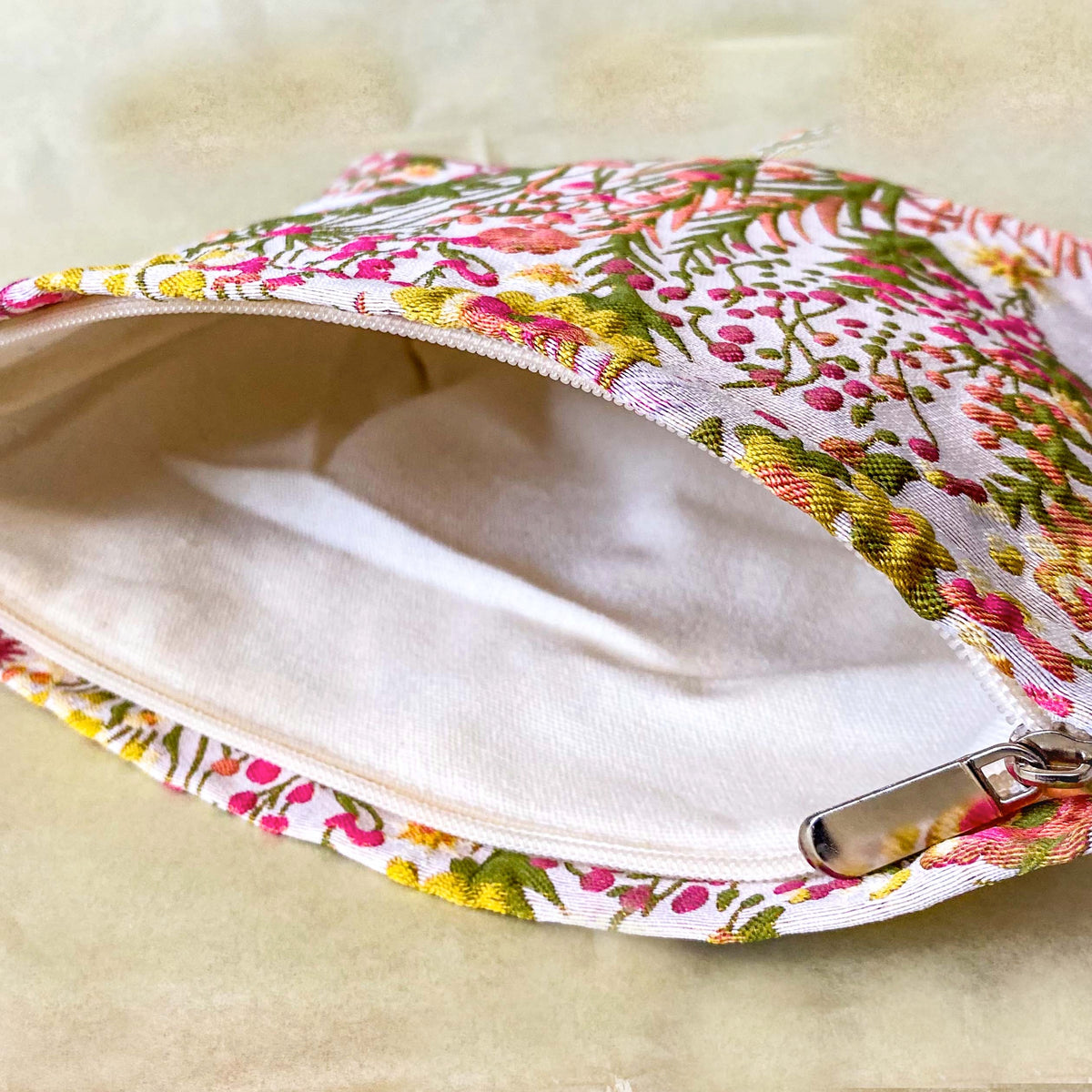 wildflower meadow tapestry pouch with colourful woven floral design including daisies, cream lining, concealed zip closure and gusseted base. Cream, orange, lemon, soft green and white design. Subtle sheen. Large cosmetic bag or toiletry pouch. Uk botanical gift shop.