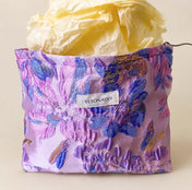 Elegant satin-finish tapestry pouch featuring woven lavender and blue florals with gold metallic thread, cream lining, concealed zip and gusseted base. Ideal for cosmetics and stationery