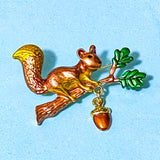 Squirrel brooch with an articulated hanging acorn on a blue background