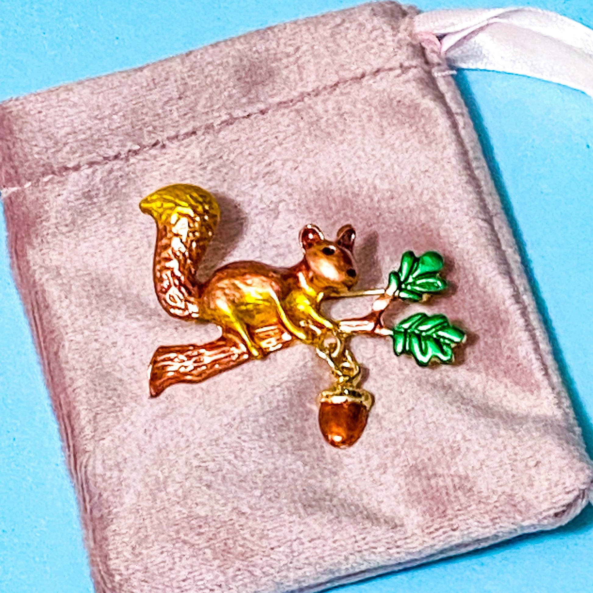 Squirrel brooch with acorn on a pink velvet bag against a blue background