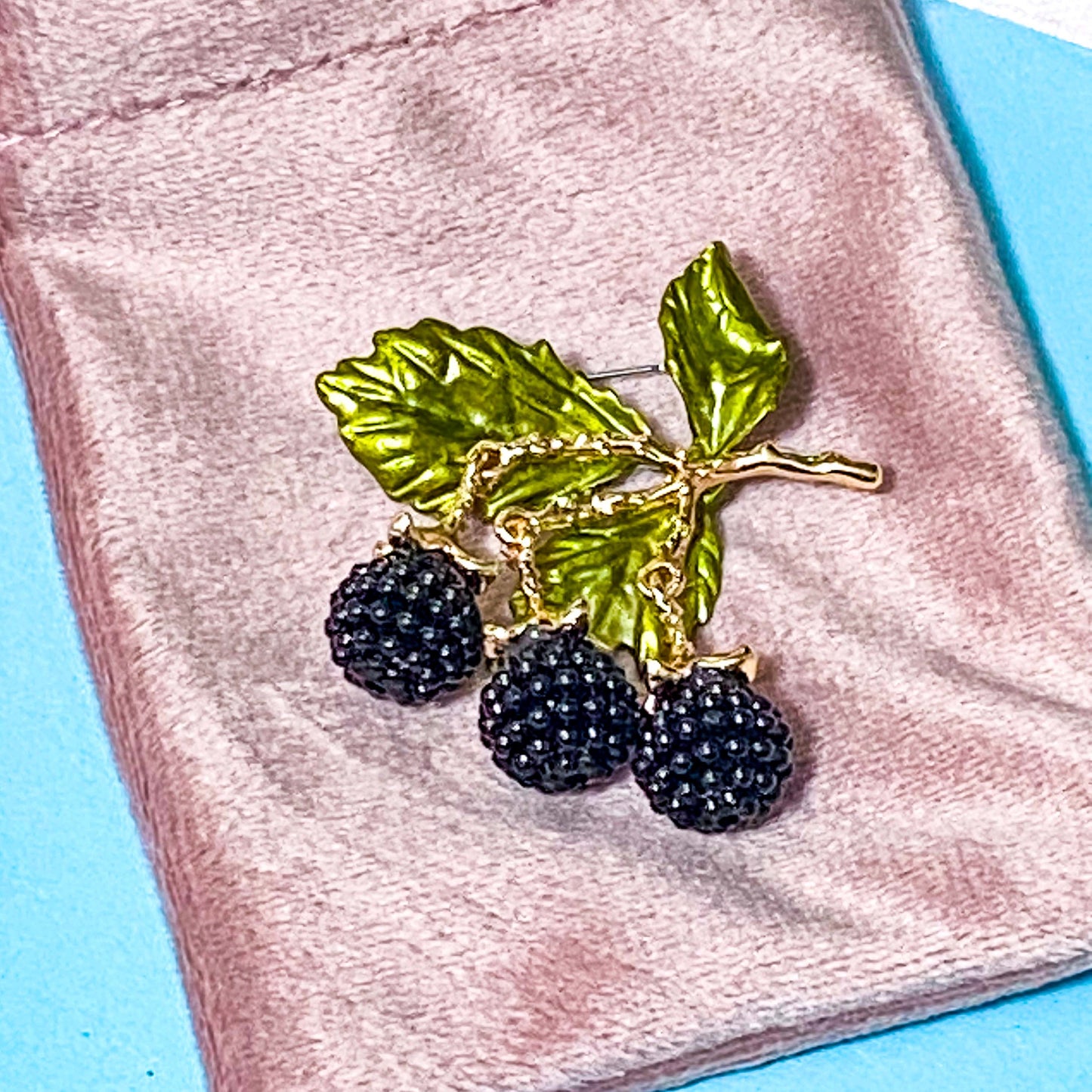wild blackberry branch articulated brooch on a pink velvet bag on a blue background
