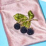 wild blackberry branch articulated brooch on a pink velvet bag on a blue background