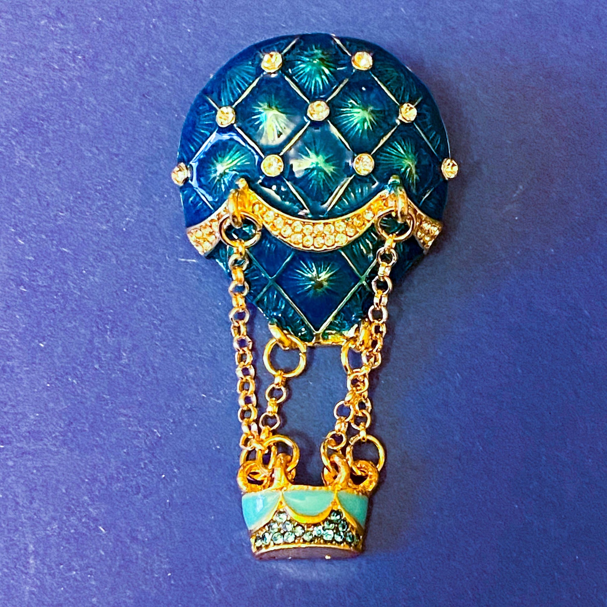 Decorative brooch shaped like a hot air balloon with blue and gold design on a blue background