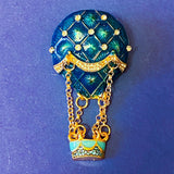 Decorative brooch shaped like a hot air balloon with blue and gold design on a blue background