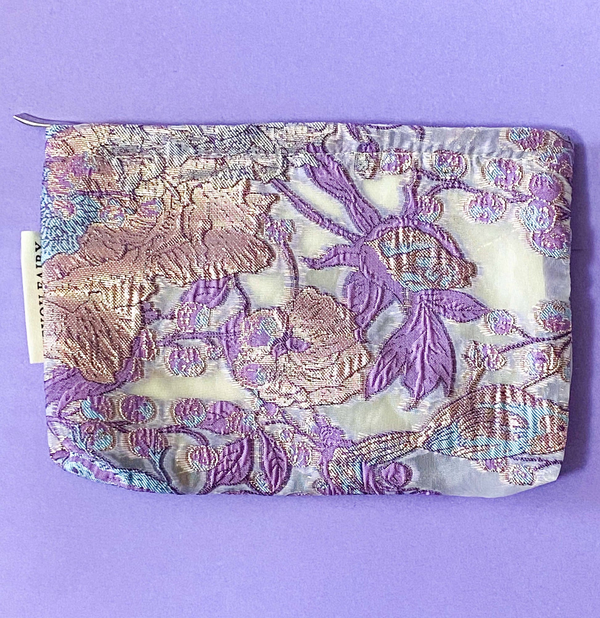 wisteria veil luxury woven tapestry cosmetic pouch with an ivory background and lavender and lilac botanical design, shimmering pale pink-lilac metallic threads, cream fabric lining and concealed zip.