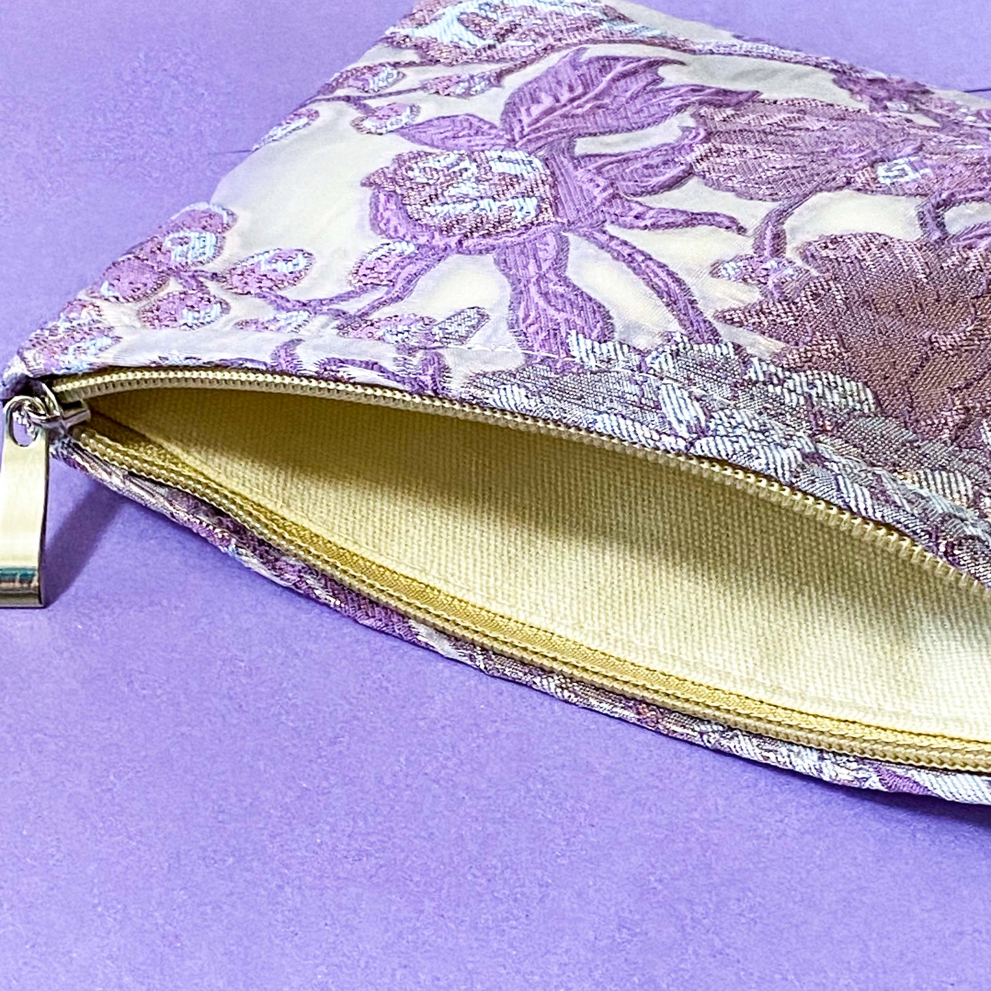 wisteria veil luxury woven tapestry cosmetic pouch with an ivory background and lavender and lilac botanical design, shimmering pale pink-lilac metallic threads, cream fabric lining and concealed zip.