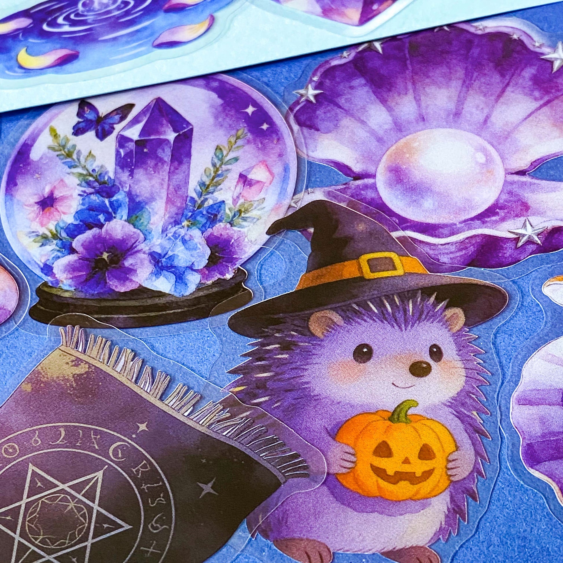 pack of 50 magical fantasy stickers featuring crystal balls, spell books, moonlit scrolls, enchanted mushrooms, ravens, potion bottles, celestial moons, magical animals and crystal gardens in lavender, violet and blue tones. UK stationery shop and letterbox gifts store.