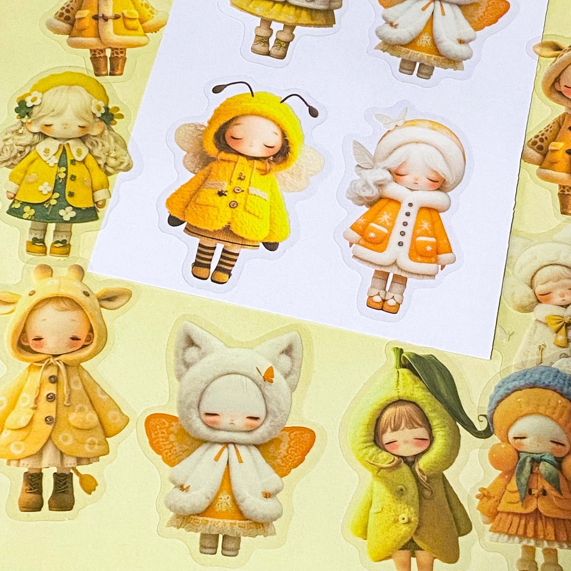 sunshine yellow and orange sticker set with 20 large PET doll stickers of girls in cute outfits and costumes, including a pea, cat, bee and giraffe. Adorable designs of cosy winter clothing and animals. 