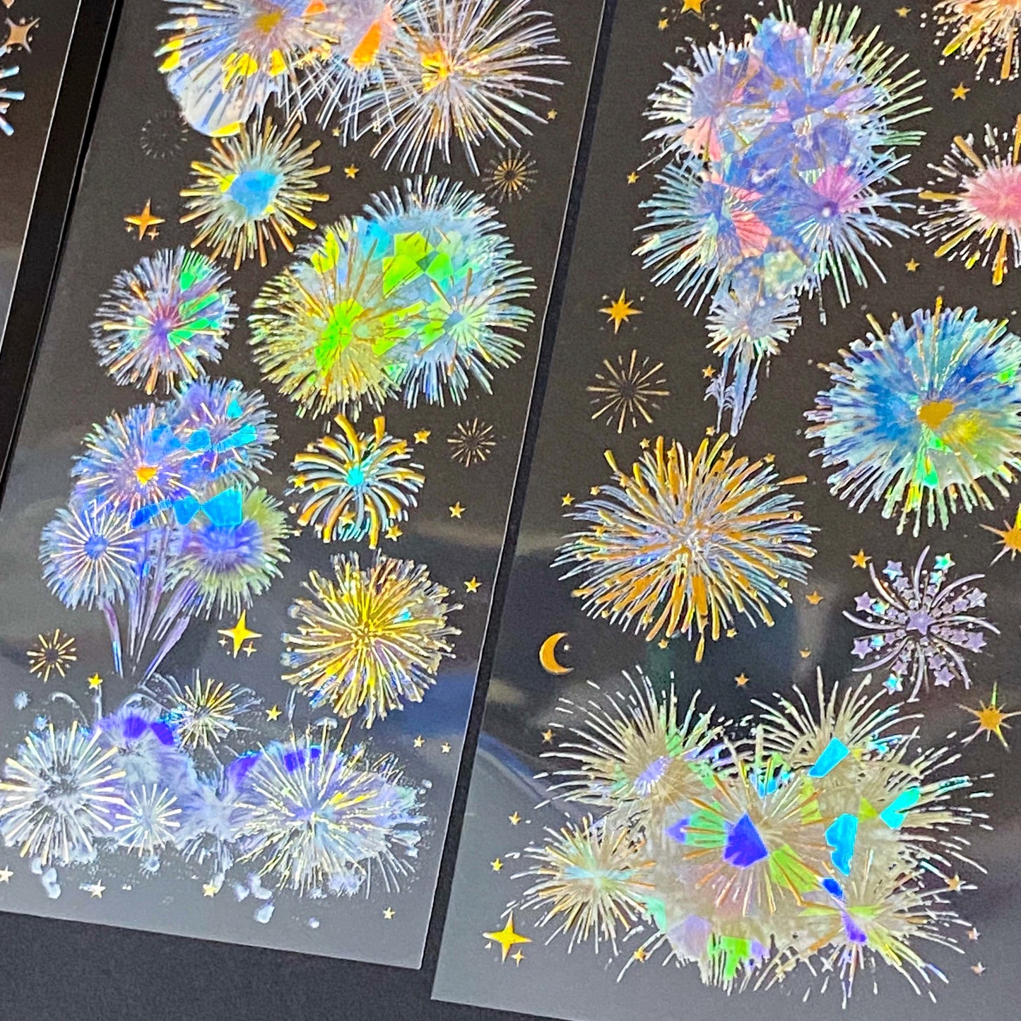 three transparent holographic firework sticker sheets with celestial stars, moons and iridescent rainbow foil effects