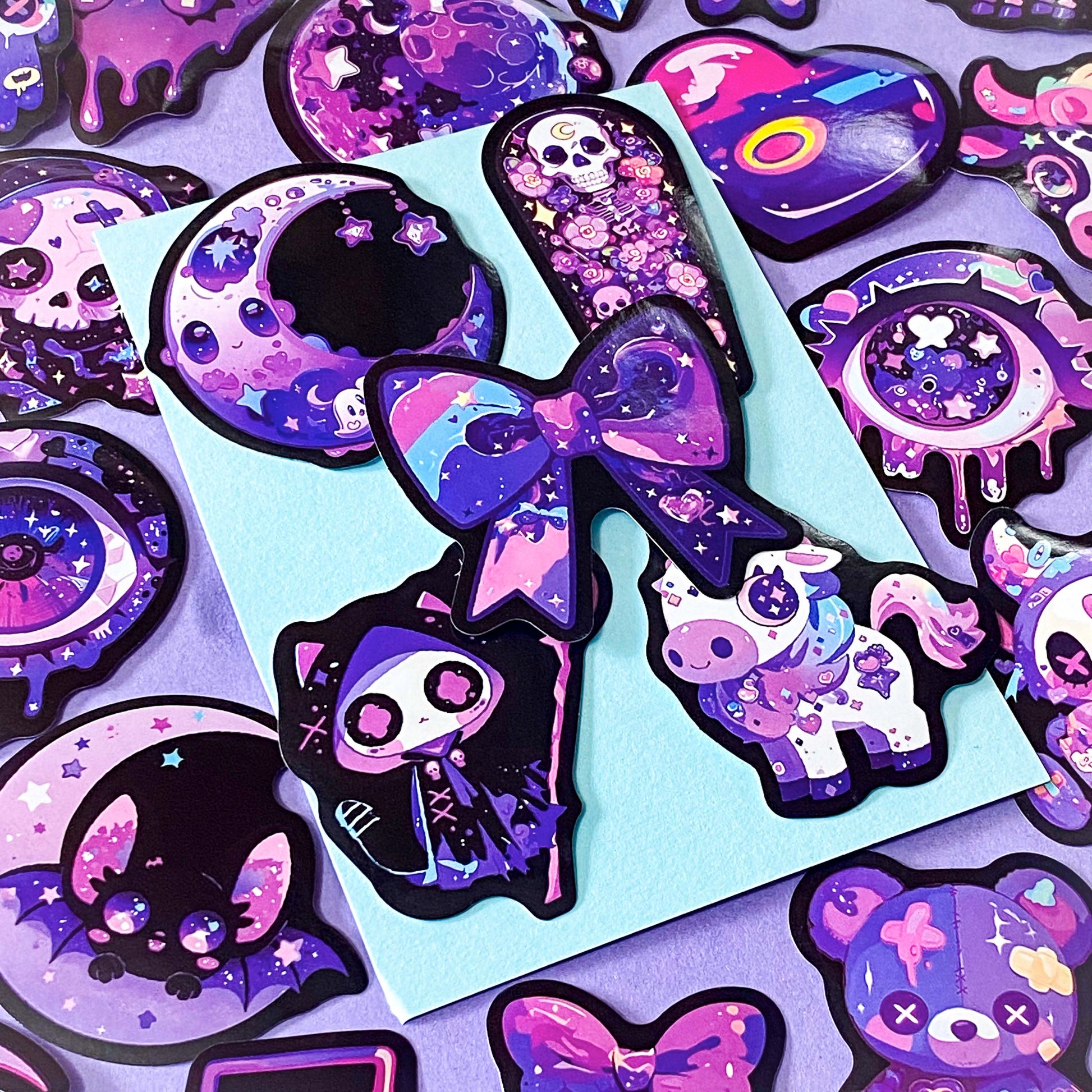 pack of 50 large glossy laptop stickers featuring bats, skulls, moons, owls, eyes, cows, unicorns, potion bottles, crystals, celestial artwork in purple, pink , lilac and blue tones. vibrant pack. uk cute stickers shop.