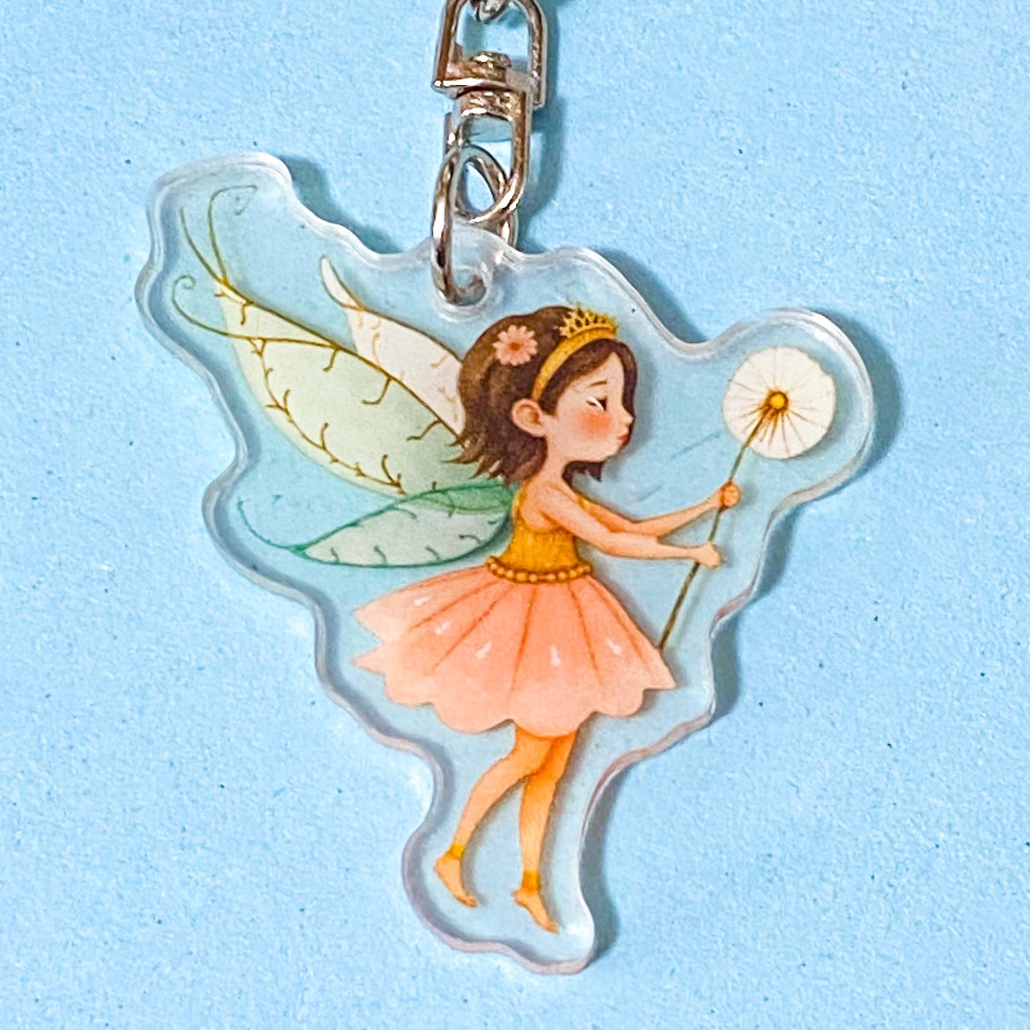 Fairy keychain with green wings and a pink dress on a light blue background