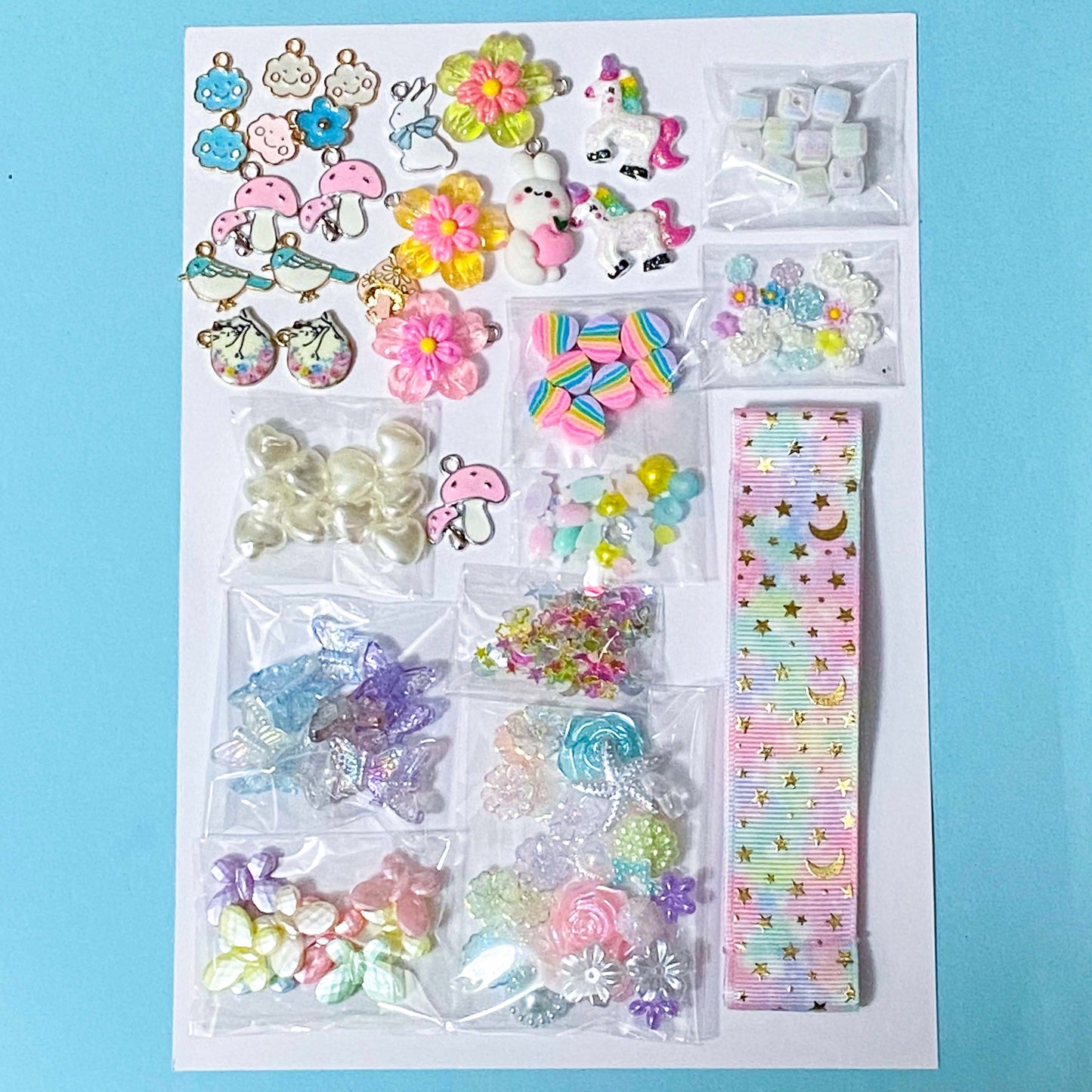 craft bundle with a kawaii cute pastel theme with beads, flatbacks, enamel charms, sequins and ribbon on a blue background