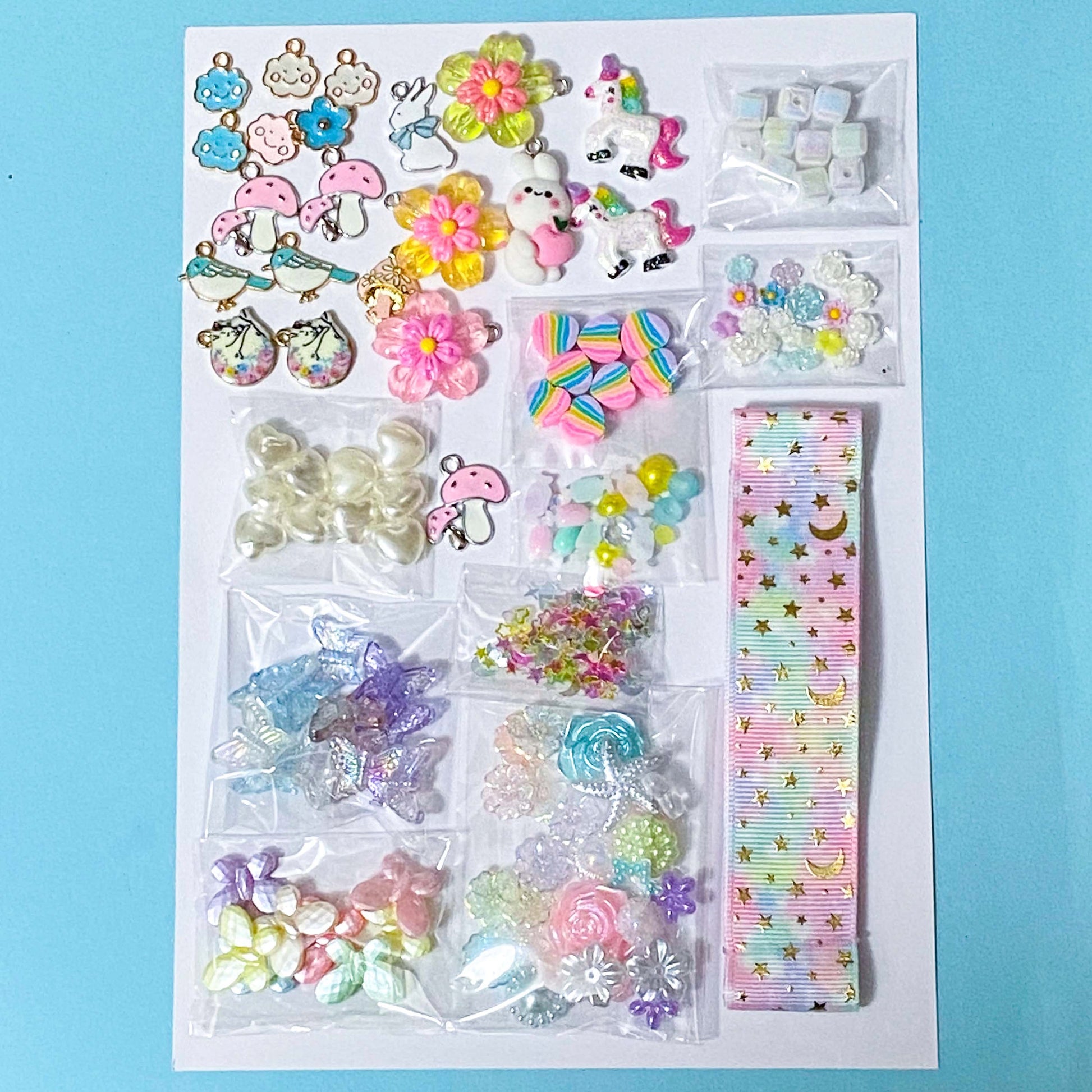 craft bundle with a kawaii cute pastel theme with beads, flatbacks, enamel charms, sequins and ribbon on a blue background