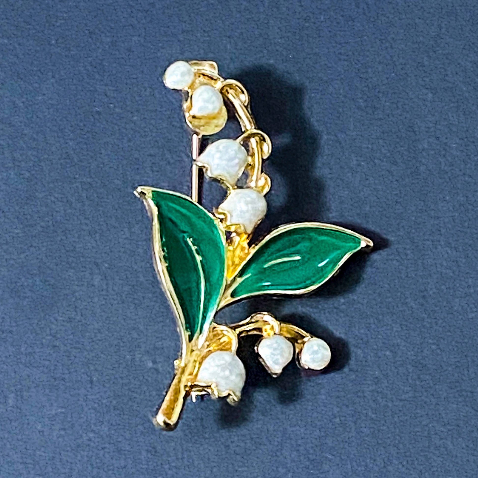 Gold lily of the valley brooch with green leaves and white flowers on a deep blue background