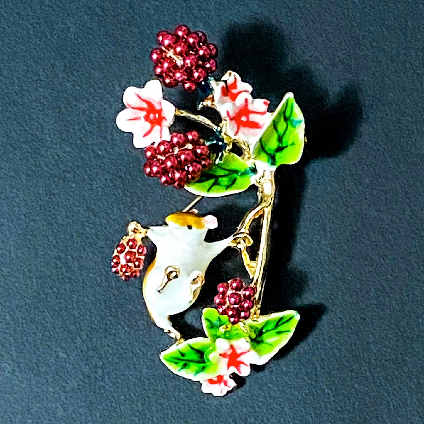 Decorative brooch with a mouse, flowers, and berries on a dark background