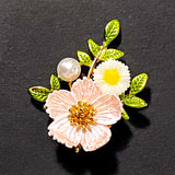 Floral brooch with a pink dog rose flower, white daisy, and pearl on a black background